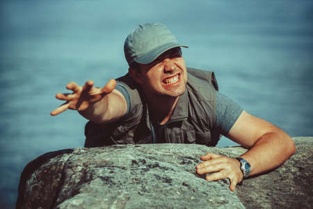 Young man tourist surviving falling from stone to water and trying to climb upの写真素材