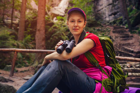 Young woman tourist in red clothing  sitting with binoculars in handの写真素材