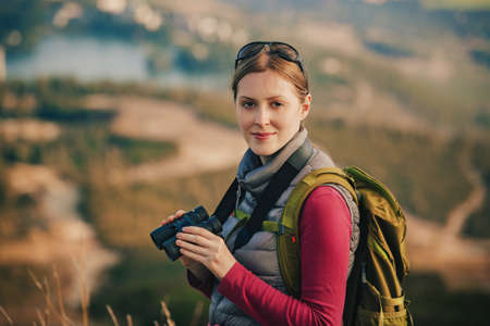 Young woman tourist standing with binoculars on mountain portraitの写真素材