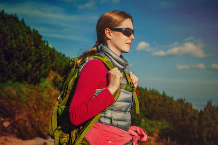 Young woman tourist with green backpack and sunglasses standing on mountains backgroundの写真素材