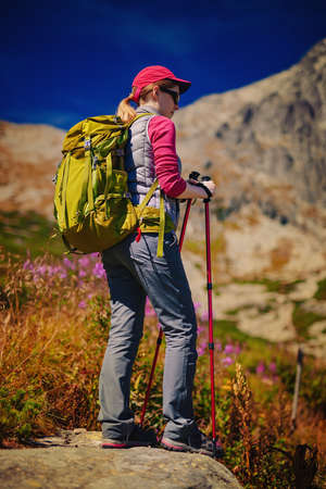 Young woman tourist with green backpack and sunglasses standing on high mountains backgroundの写真素材