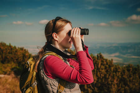 Young woman tourist with binoculars looking on mountainsの写真素材