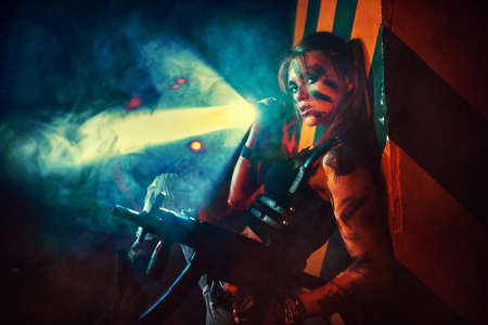 Young strong woman warrior with gun and flashlight in dramatic urban night sceneの写真素材