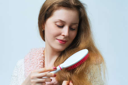 Young blond woman in bathrobe comb hair after washing. On white background.