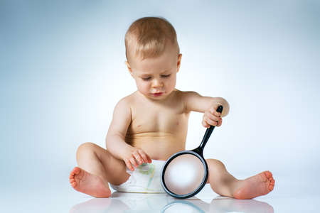 Eight month baby sitting and playing with magnifier on white backgroundの写真素材