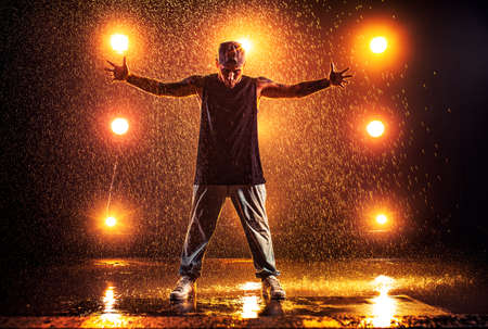 Young man break dancer standing in club with lights and water. Tattoo on body.