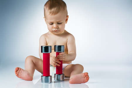 Eight month baby sitting and playing with dumbbells on white backgroundの写真素材