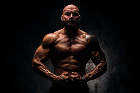Strong man bodybuilder on dark background. Dramatic colors. Tattoo on body.