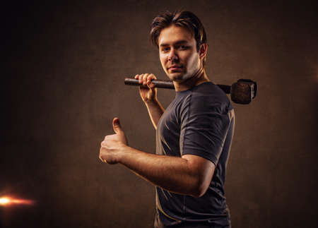 Young strong man with hammer on wall backgroundの写真素材