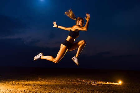 Young sports woman high jumping outdoors twilight trainingの写真素材
