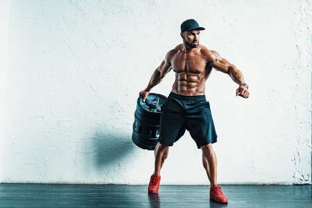 Young strong man bodybuilder with big barrel in hand looking asideの写真素材