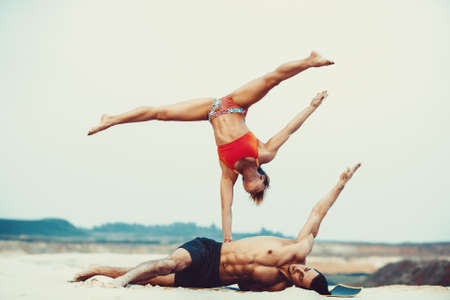 Young sports couple doing acroyoga exercises on sand beachの写真素材
