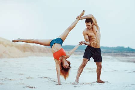 Young sports couple doing acroyoga exercises on sand beach. Bright white colors.の写真素材