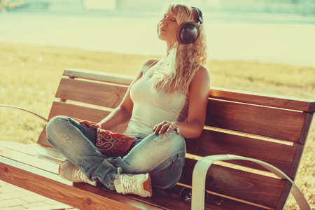 Young teenage style woman sitting on bench at morning and listening music. Warm sunny light.の写真素材