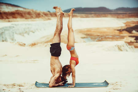Young sports couple doing acroyoga exercises on sand beach. Standing upside down.の写真素材