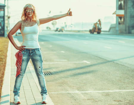 Young teenage style woman with sunglasses standing at the city road with thumbs up handsign.の写真素材