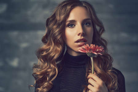 Young woman with flower and curly hair portrait in soft colorsの写真素材