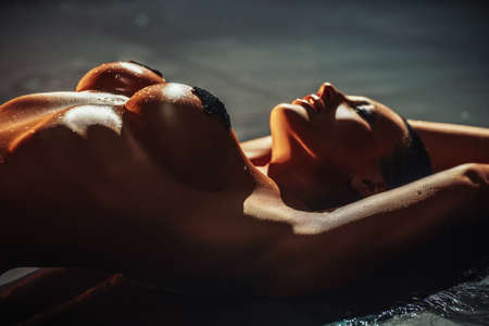 Young sexy naked woman posing in pool with water. Dark contrast  warm colors. Shallow focus depth.の写真素材