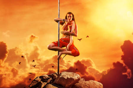 Young woman exotic style pole dancing with snake on mountain top. Asian style and red warm colors....