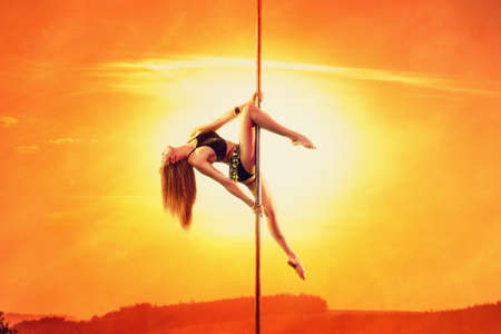 Young woman exotic style pole dancing on sunset sky and sun warm red background. Asian style clothing. の写真素材