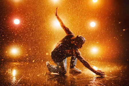 Young man break dancing in club with lights and water. Tattoo on body.の写真素材