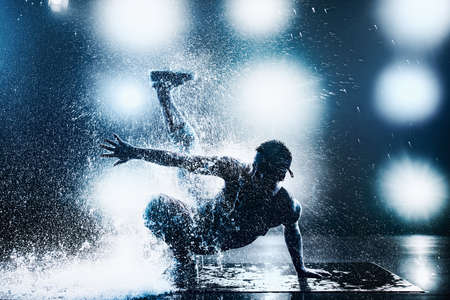 Young man break dancing in club with lights and water. Tattoo on body. Blue tint colors.の素材 [FY31091247253]