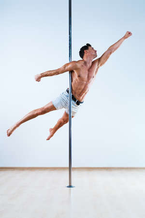 Young pole dancing man on white and blue wall backgroundの写真素材