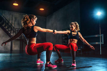 Young slim sports twins girl team training in big hall dark interiorの写真素材