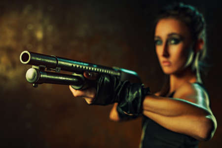 Young strong woman with gun in dramatic dark interior. Focus on gun.の写真素材