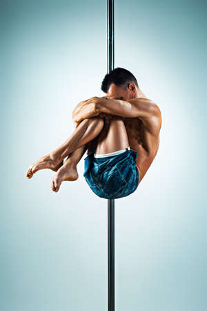 Young strong man pole dancing on blue and white backgroundの写真素材