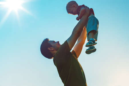 Father with one year son. Holding son up to the sunset light.の写真素材