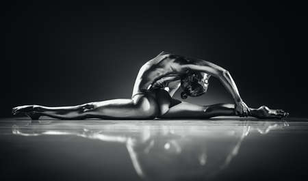 Young topless woman stretching. Silver body paint and toning for metallic skin effect. Dramatic colors.の写真素材
