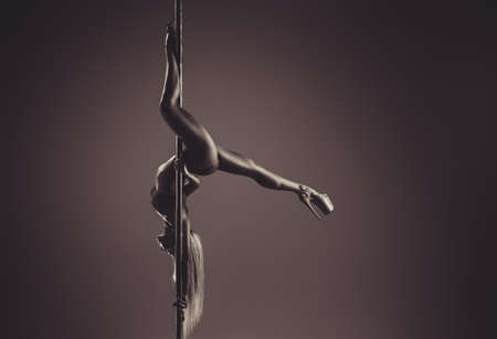 Young slim sexy woman pole dancing upside down on wall background. Warm sepia tint.の写真素材