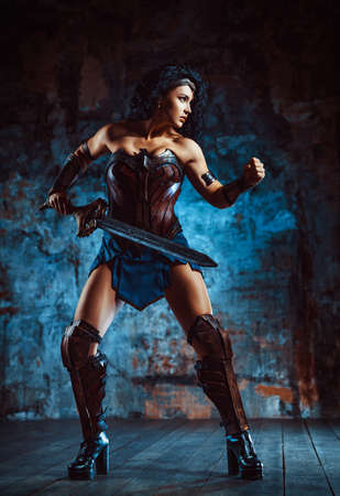 Young brunette woman warrior with sword on stone wall backgroundの写真素材