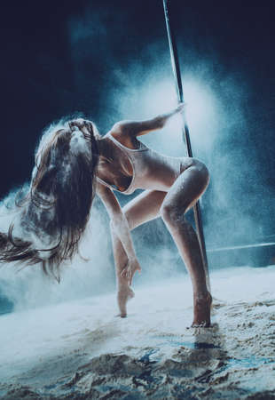 Young sexy woman pole dancing on dark background with flour and dust effect.の写真素材