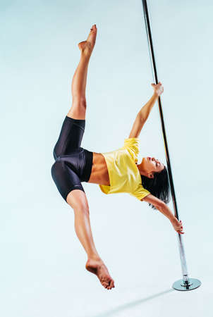 Young slim woman pole dancing on white background