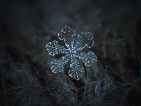 Snowflake on dark textured background: macro photo of real snow crystal on black woolen fabric in natural light. This is very large, but simple snowflake of with broad arms and tiny central hexagon.の写真素材