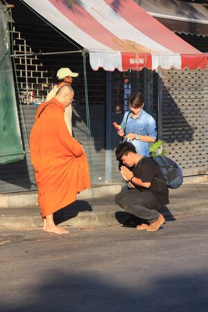 Two people make a merit to monk on the street in the morning while monk's assistant are waiting.のeditorial素材