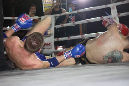 two muay thai fighter fell down on the stage in theri fight while people was taken this photo shot.のeditorial素材