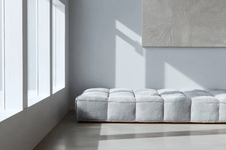 A spacious living room features a sleek gray couch resting against a wall. Bright natural light streams through large windows, illuminating the minimalist design and artwork above.の素材