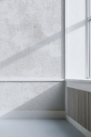 Sunlight pours into a minimalist room, highlighting textured white walls and clean lines. The corner features a sleek radiator and offers a tranquil atmosphere.の素材
