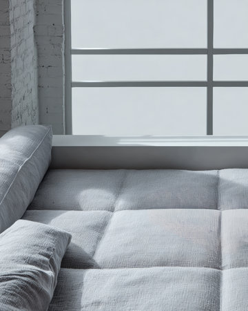A comfortable gray sofa with plush cushions sits next to a large window. Sunlight streams in, illuminating the soft texture of the fabric and the serene ambiance of the room.の素材