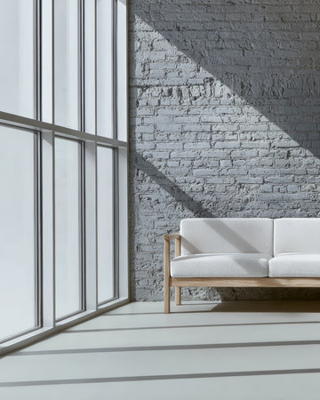 A minimalistic living room features a comfortable white sofa beside large windows. Bright sunlight floods the space, casting shadows on the gray brick wall, creating an inviting atmosphere.の素材