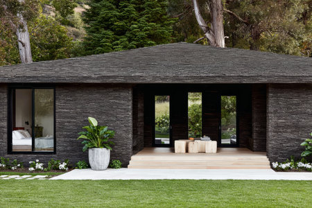 This contemporary stone house features a sleek design with large windows and a welcoming porch. The surrounding garden has well-maintained grass and plants, adding to the peaceful atmosphere.の素材