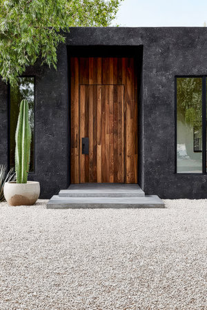 This entryway features a sleek wooden door framed by black walls, accompanied by desert plants. Loose gravel adds a natural touch to the serene outdoor space.の素材