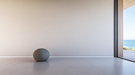 A simple and modern room features a round object in the center. Large windows reveal a stunning view of the ocean and blue sky, creating a serene atmosphere.の素材