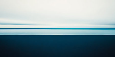 An expansive view showcases the ocean meeting the sky at the horizon. The calm water reflects shades of blue and gray under cloudy skies, creating a serene atmosphere.の素材