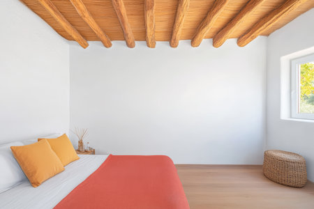 A bright, inviting bedroom features a cozy bed with orange and white bedding, a natural wood ceiling, and a simple decorative basket.の素材