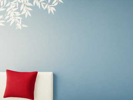 A cozy room features a light blue wall adorned with white leaf patterns. A bright red cushion rests on a white sofa, enhancing the inviting and relaxed ambiance.の素材