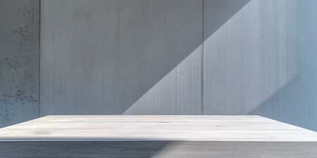 Bright sunlight illuminates a simple wooden table, creating a strong diagonal shadow on the sleek wall behind. The scene highlights minimalism and natural light.の素材
